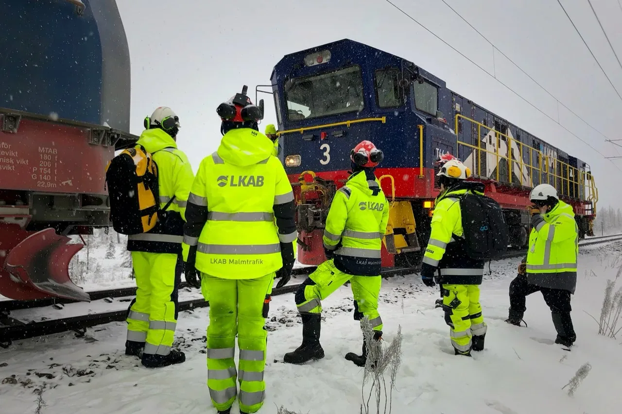 En grupp personer i varselkläder står vid tågspår. 