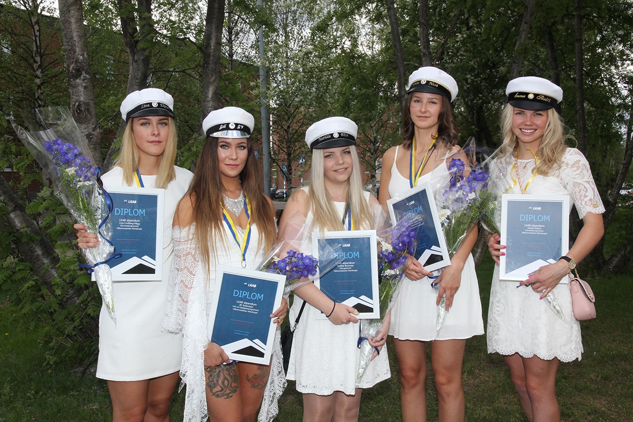Fem kvinnliga studenter med diplom och blommor iklädda vita kl