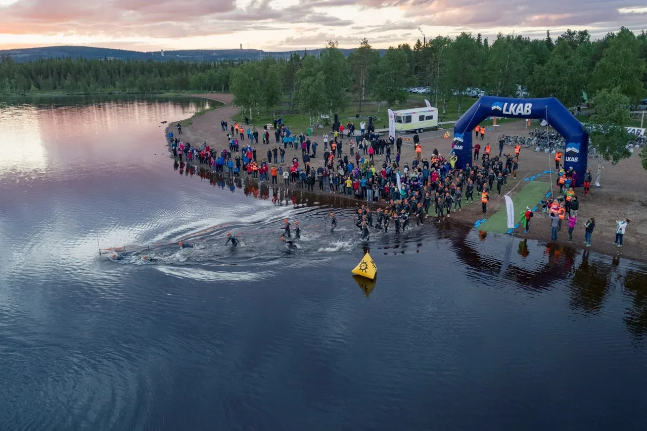 En stor grupp människor simmar ut från strand. 