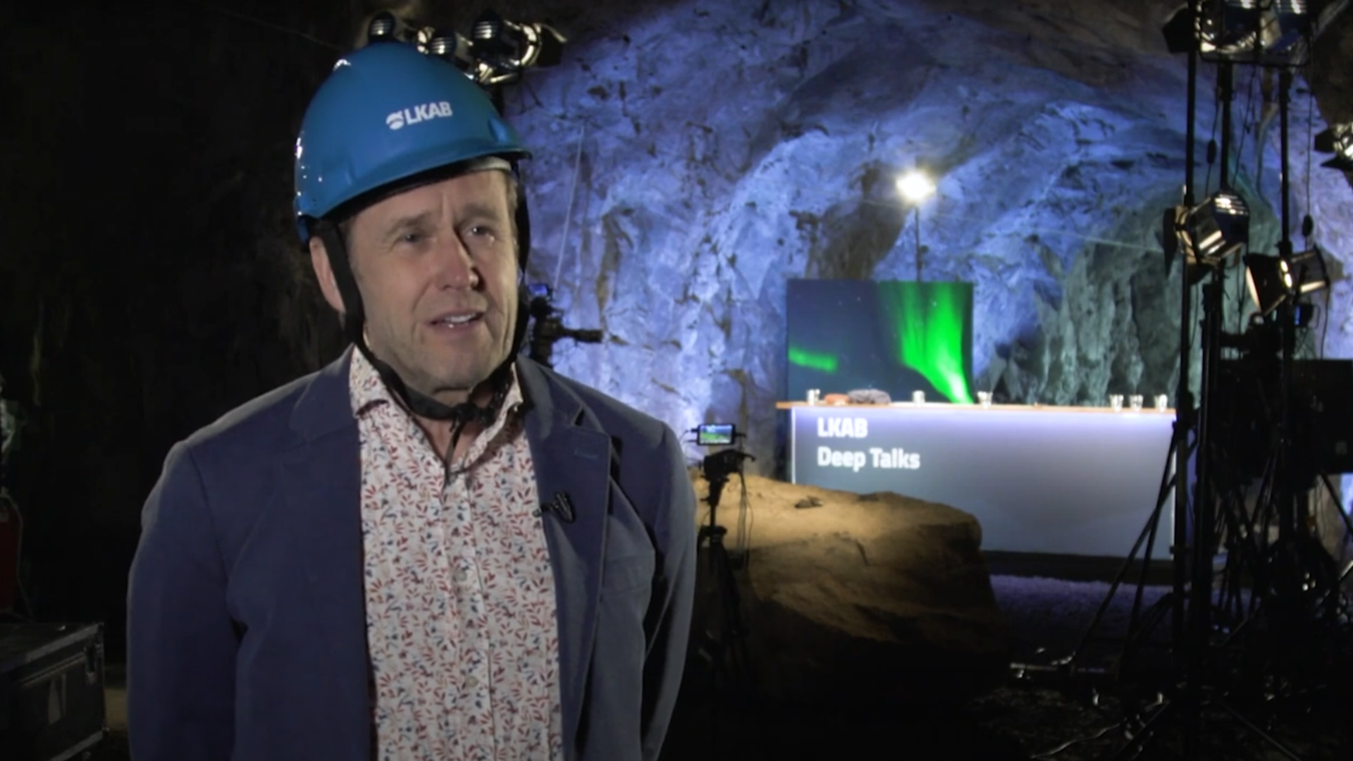 Man in mining helmet, under ground, with tv studio in background