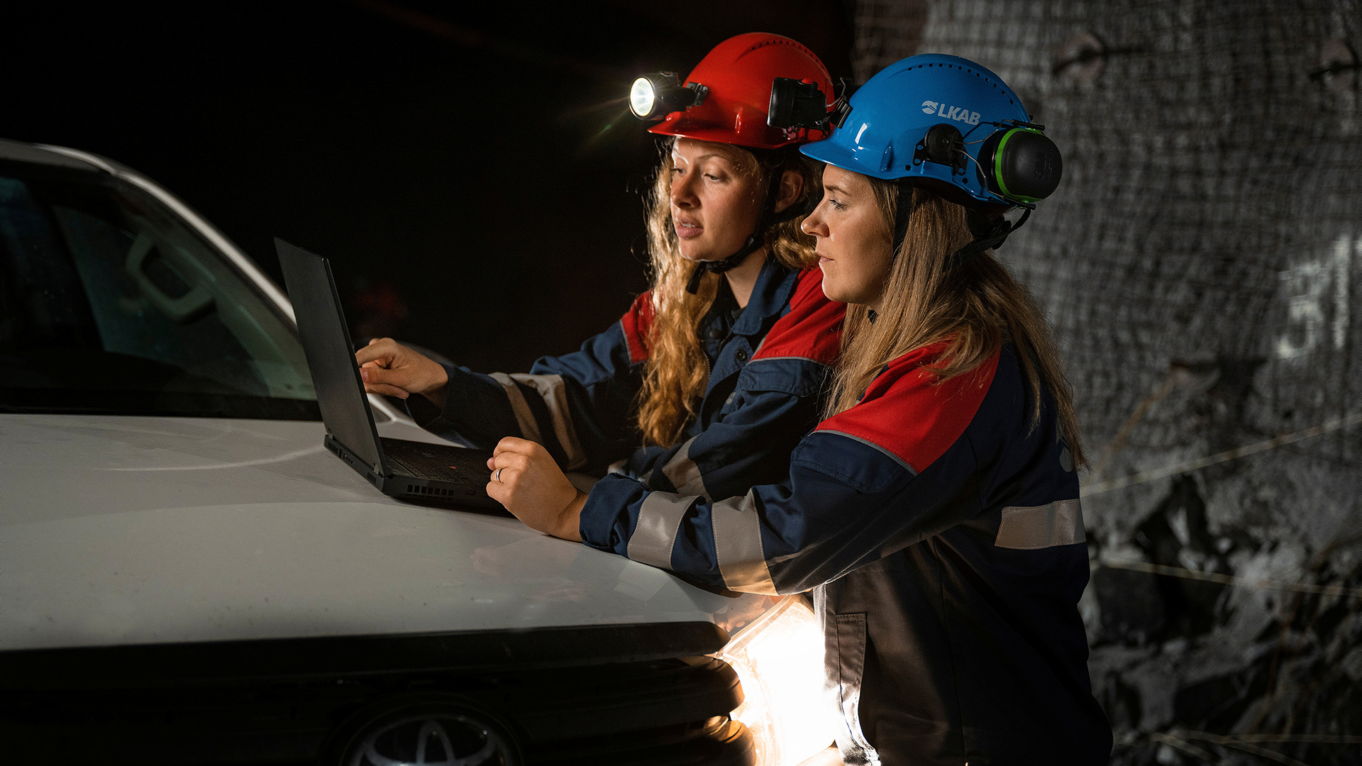 Två kvinnor i arbetskläder tittar på en dator i underjordsmiljö