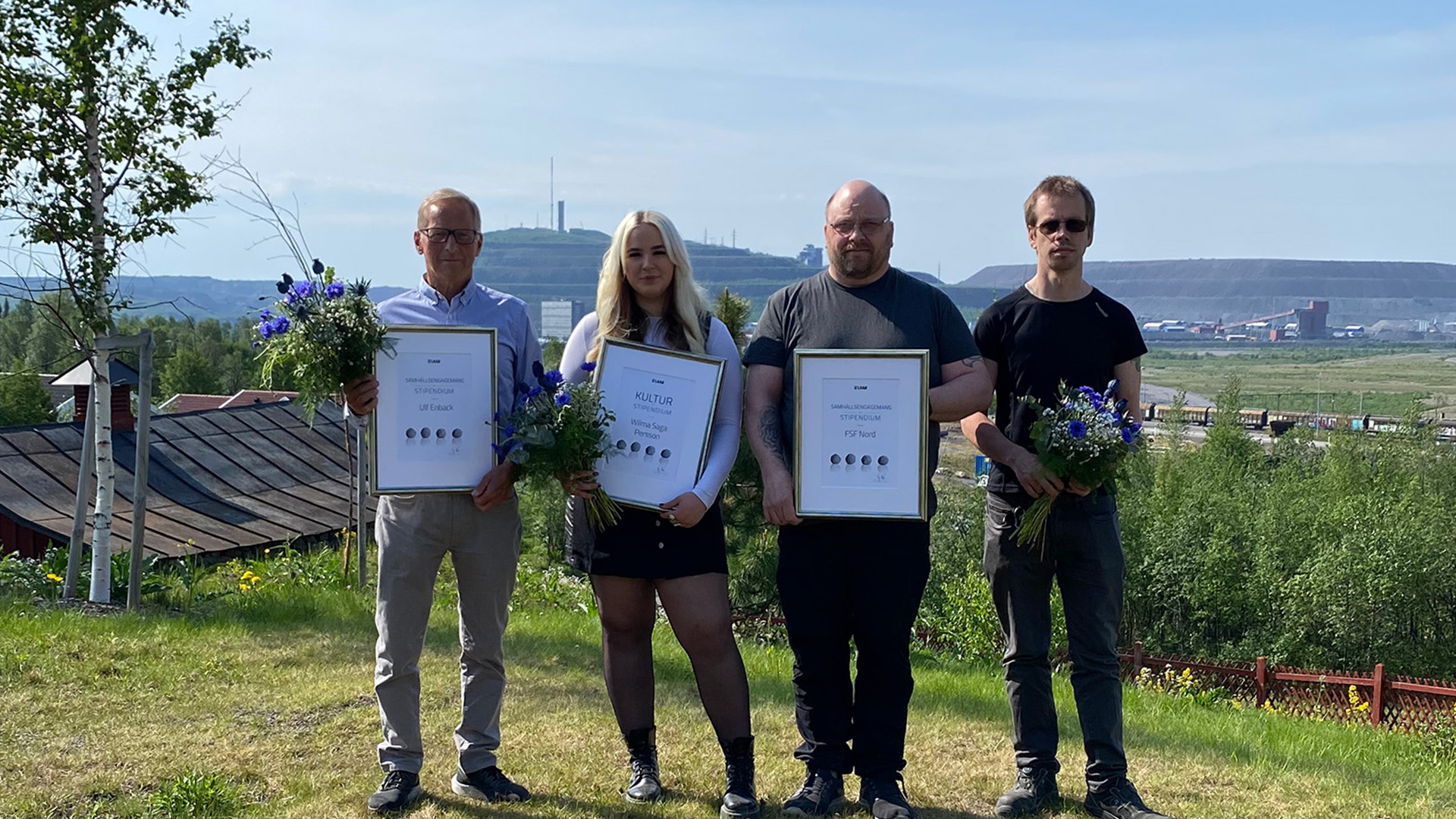 Group of people holding diplomas and flowers.
