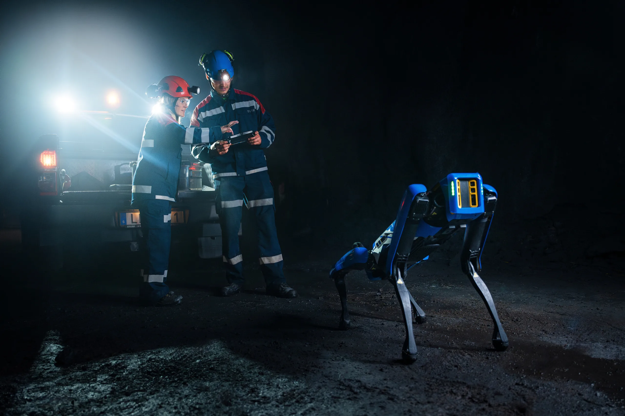 Två personer i arbetskläder och robothund i underjordsmiljö