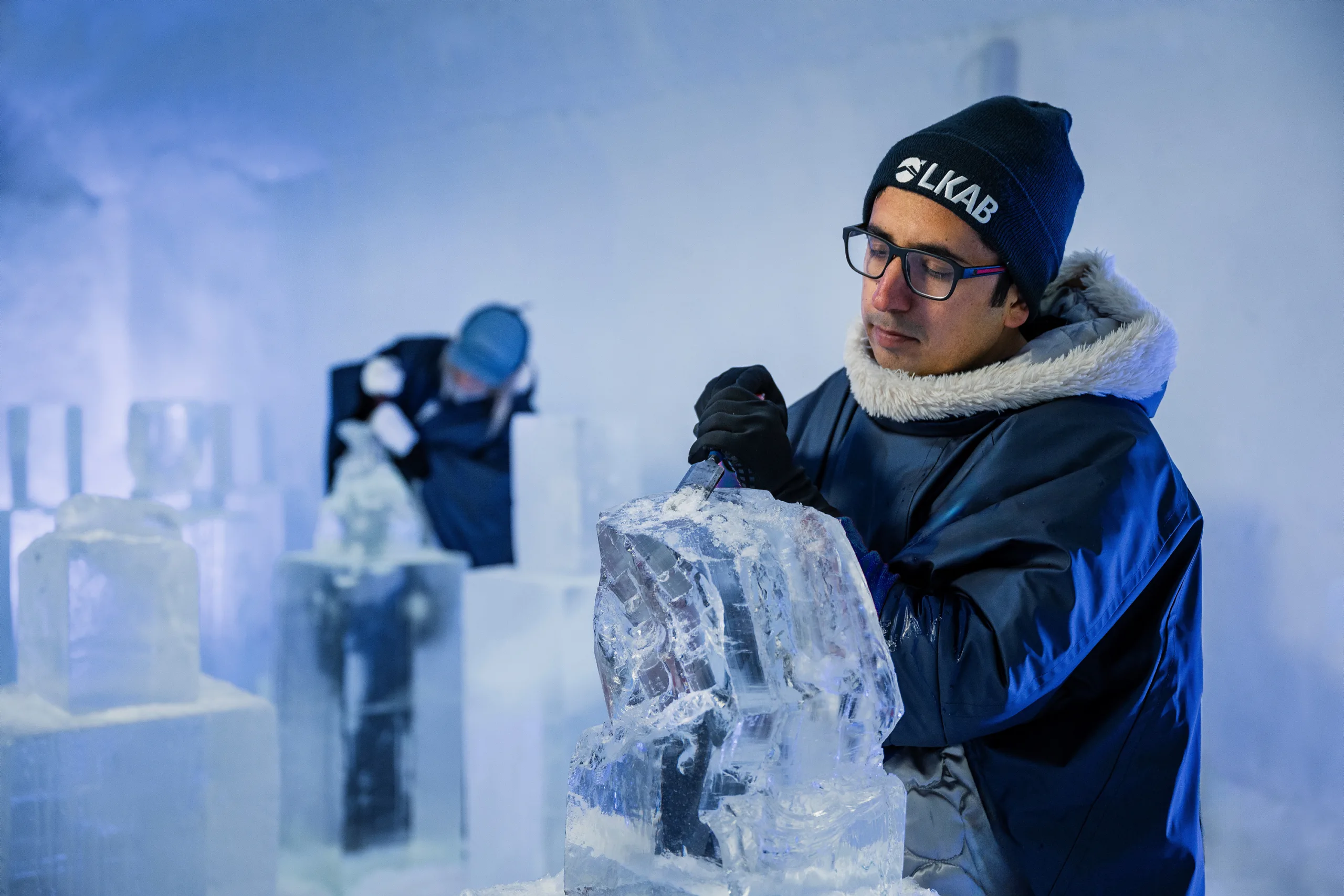 Man i vinterkläder skulpterar i is.